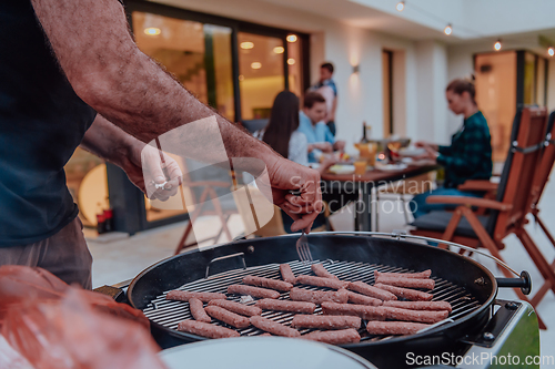 Image of A group of friends and family barbecue together in the evening on the terrace in front of a large modern house