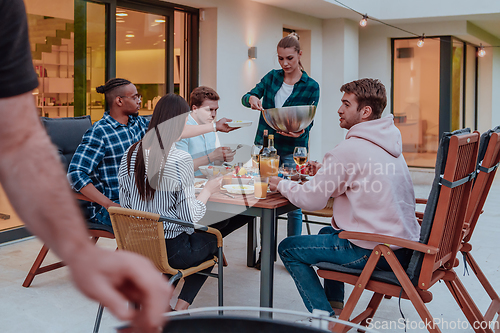 Image of A group of young diverse people having dinner on the terrace of a modern house in the evening. Fun for friends and family. Celebration of holidays, weddings with barbecue.