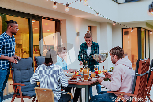 Image of A group of young diverse people having dinner on the terrace of a modern house in the evening. Fun for friends and family. Celebration of holidays, weddings with barbecue.