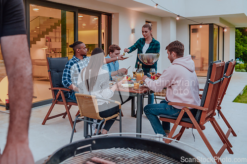 Image of A group of young diverse people having dinner on the terrace of a modern house in the evening. Fun for friends and family. Celebration of holidays, weddings with barbecue.