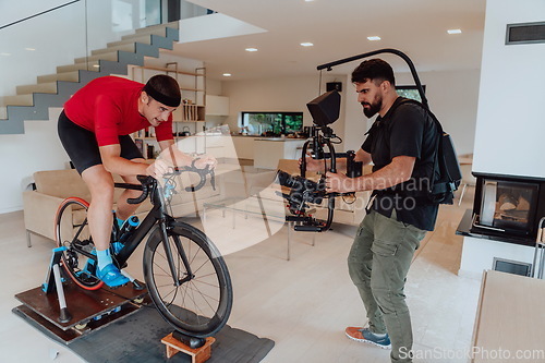 Image of A cameraman filming an athlete riding a triathlon bike on a simulation machine in a modern living room. Training in pandemic conditions.