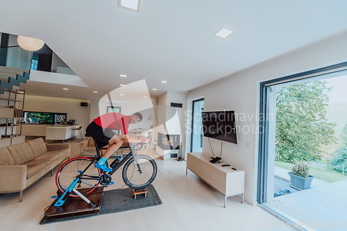 Image of A man riding a triathlon bike on a machine simulation in a modern living room. Training during pandemic conditions.