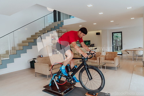 Image of A man riding a triathlon bike on a machine simulation in a modern living room. Training during pandemic conditions.