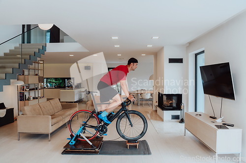 Image of A man riding a triathlon bike on a machine simulation in a modern living room. Training during pandemic conditions.