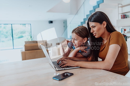 Image of Mother with her daughter talking on laptop with family and friends while sitting in modern living room of big house