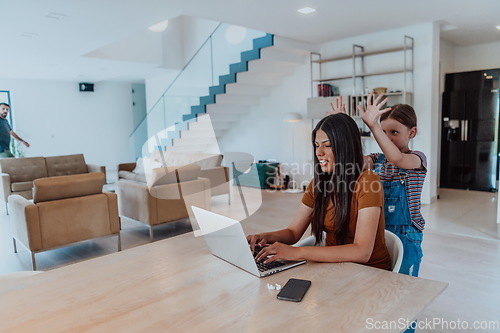 Image of Mother with her daughter talking on laptop with family and friends while sitting in modern living room of big house