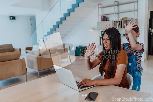 Image of Mother with her daughter talking on laptop with family and friends while sitting in modern living room of big house