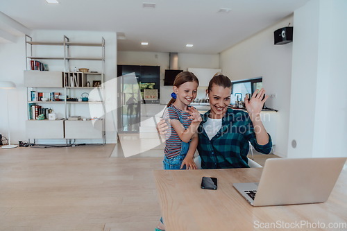 Image of Mother with her daughter talking on laptop with family and friends while sitting in modern living room of big house