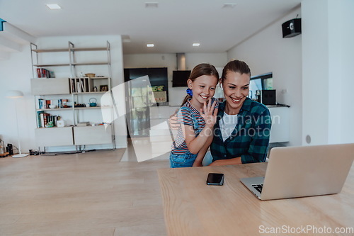 Image of Mother with her daughter talking on laptop with family and friends while sitting in modern living room of big house