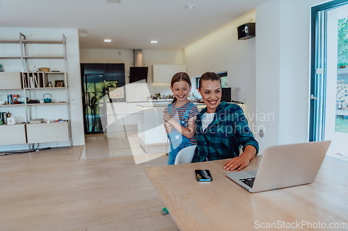 Image of Mother with her daughter talking on laptop with family and friends while sitting in modern living room of big house