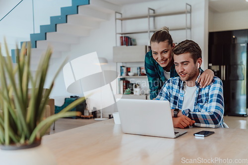 Image of A young married couple is talking to parents, family and friends on a video call via a laptop while sitting in the living room of their modern house