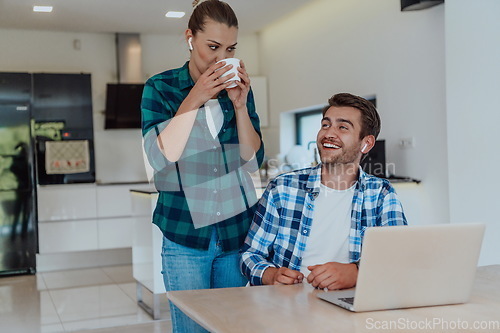 Image of A young married couple is talking to parents, family and friends on a video call via a laptop while sitting in the living room of their modern house