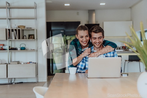 Image of A young married couple is talking to parents, family and friends on a video call via a laptop while sitting in the living room of their modern house