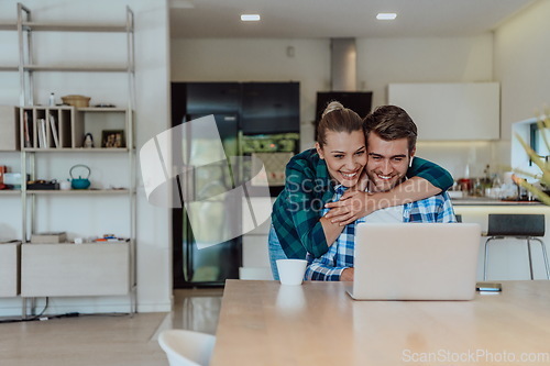 Image of A young married couple is talking to parents, family and friends on a video call via a laptop while sitting in the living room of their modern house