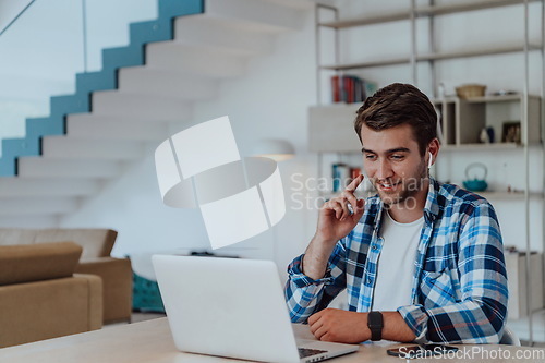 Image of The man sitting at a table in a modern living room, with headphones using a laptop for business video chat, conversation with friends and entertainment