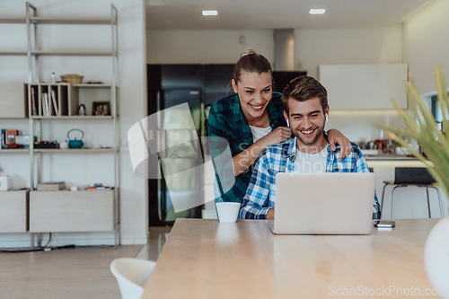 Image of A young married couple is talking to parents, family and friends on a video call via a laptop while sitting in the living room of their modern house