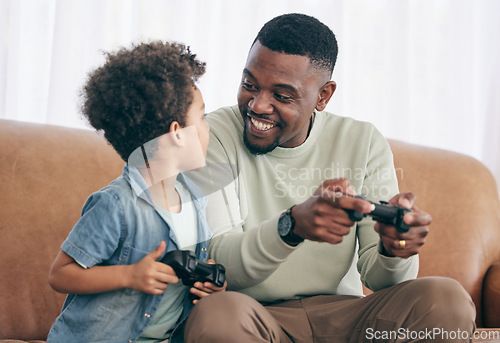 Image of Black family, father and child playing video games on living room sofa together with controllers at home. Happy African American dad with son with smile enjoying bonding time on console entertainment