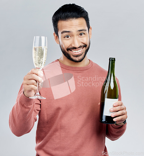 Image of Portrait, champagne and toast with a man in studio on a gray background holding a bottle for celebration. Glass, alcohol and cheers with a handsome young man celebrating the new year tradition