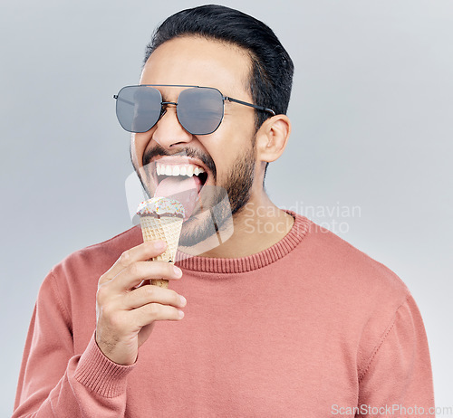 Image of Summer, sunglasses and ice cream with a man in studio on a gray background enjoying a sweet, treat or snack. Food, fashion and dessert with a handsome young male eating or licking an icecream cone