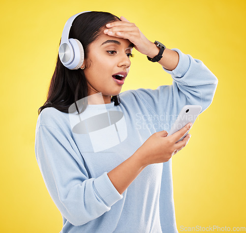 Image of Shock, surprise and woman with phone, headphones and hand on head isolated on yellow background. Social media, music news or exciting online gossip, hispanic girl reading notification on smartphone.