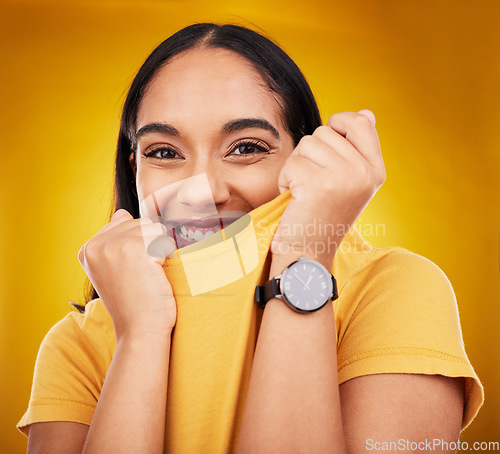 Image of Portrait, shy and playful with a woman on a yellow background in studio pulling on her t-shirt. Face, fashion or funny and an attractive young female covering her mouth with trendy clothes for style