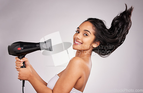 Image of Portrait, blow dry and hair with a model woman in studio on a gray background holding an appliance. Salon, smile and hairdryer with an attractive young female drying her hairstyle for beauty