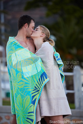 Image of Sea, kiss and young couple in beach towels with love and bonding after engagement outdoor. Vacation travel, trust and happiness of a woman and man together by a ocean in nature sharing a sweet moment