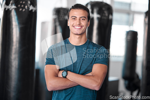 Image of Portrait, punching bag with a man boxer in the gym, standing arms crossed for fitness or motivation. Happy, exercise and confidence with a handsome young male training for boxing or a fight