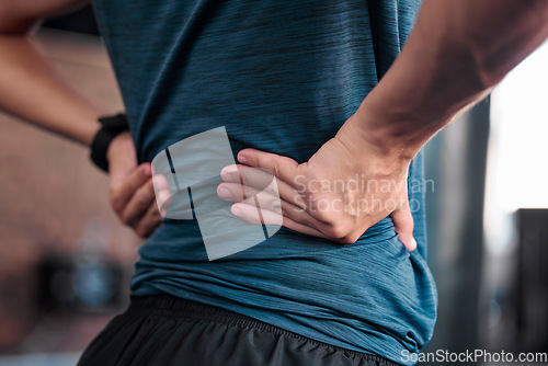 Image of Hands, back and injury with a sports man holding a muscle in pain while training in a gym for health. Fitness, accident and anatomy with a male athlete suffering from an injured body during exercise