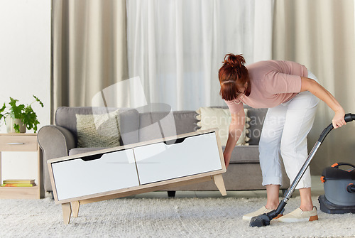 Image of Woman, vacuum and housekeeping on carpet in living room for spring cleaning service, dust or dirt removal at home. Female cleaner lifting table and vacuuming for clean rug, mat or floor in the lounge