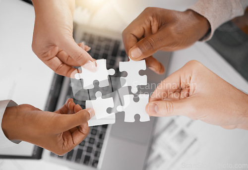 Image of Hands, puzzle piece and overhead with a business team in the office, working in collaboration on a project. Teamwork, jigsaw and laptop with a diverse group of people at work together from above