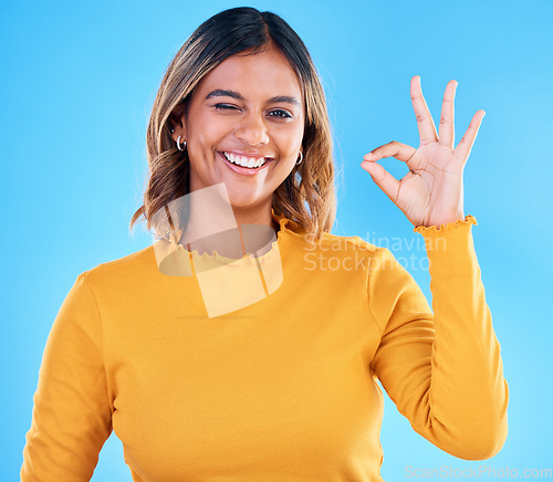 Image of Ok, portrait and happy woman wink on blue background, studio and agreement of support. Female model, smile and okay hands of success, yes and winner of perfect emoji, thank you and review approval
