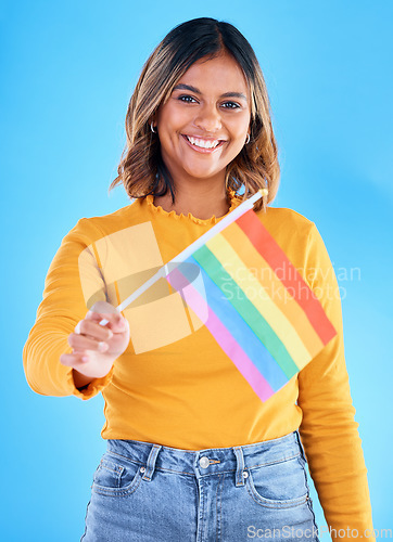 Image of Portrait, flag and gay pride with a woman on a blue background in studio feeling proud of her lgbt status. Smile, freedom and equality with a happy young female holding a symbol of inclusion