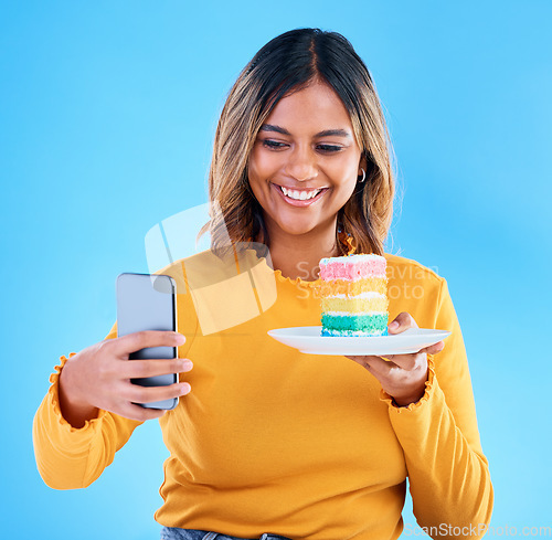 Image of Woman, cake and studio with a selfie and smile for social media while excited to eat. Happy female on blue background with rainbow color dessert for influencer birthday celebration profile picture