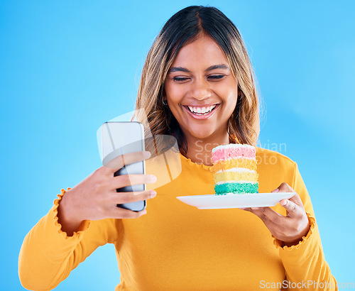 Image of Woman, cake and smile selfie in studio for social media profile picture and excited to eat. Happy female laughing on blue background with rainbow color dessert for birthday or influencer celebration