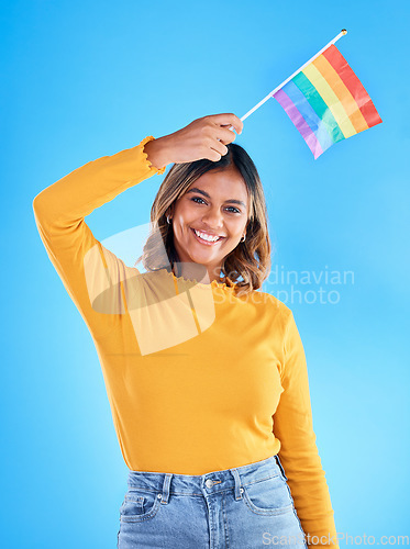 Image of Portrait, rainbow flag and gay pride with a woman on a blue background in studio feeling proud of her lgbt status. Smile, freedom and equality with a happy young female holding a symbol of inclusion