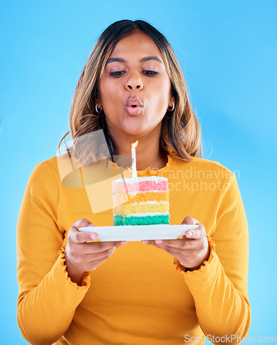 Image of Birthday cake, woman and blow candles in studio, blue background and celebration. Female model, dessert and wishing at party, flame and special event, rainbow treat or celebrate happiness on backdrop