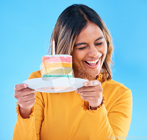 Image of Woman, birthday cake and candle studio with a smile and excited to eat. Happy female person laughing on blue background with sweet rainbow color dessert for celebration and happiness on face