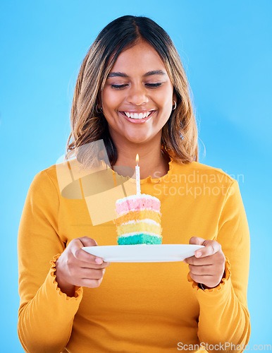 Image of Birthday cake, happy party and woman in studio, blue background and celebration. Female model, rainbow dessert and candle of special event, sweets and smile to celebrate happiness, wish and surprise