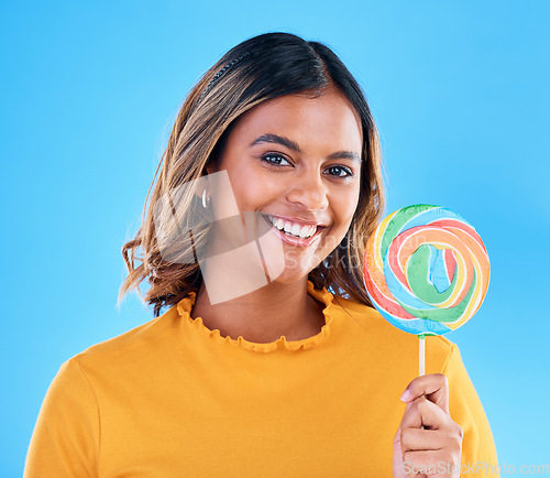 Image of Portrait, lollipop and a woman on a blue background in studio wearing heart glasses for fashion. Smile, candy and sweet with an attractive young female eating a giant snack while feeling happy