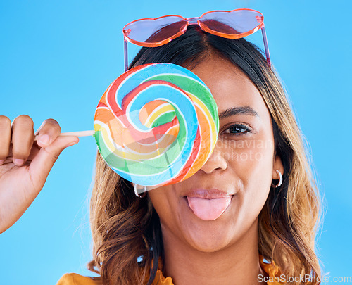 Image of Portrait, lollipop and tongue with a woman on a blue background in studio wearing heart glasses for fashion. Funny face, candy and sweet with a young female eating a giant snack while feeling silly