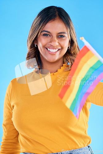 Image of Portrait, flag and gay with a woman on a blue background in studio feeling proud of her lgbt status. Smile, freedom and equality with a happy young female holding a rainbow symbol of inclusion