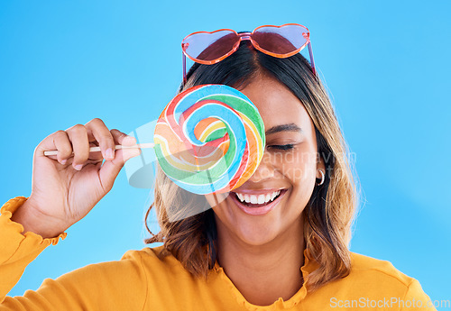 Image of Laughing, lollipop and a woman on a blue background in studio wearing heart glasses for fashion. Funny, candy and sweet with an attractive young female eating a giant snack while feeling silly