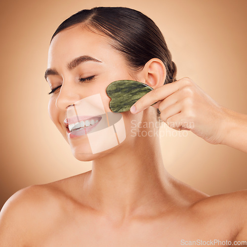 Image of Skincare, gua sha stone and woman face cleaning of a young person with happiness in a studio. Happy smile and dermatology treatment of a female with cosmetics, spa and cosmetology luxury facial