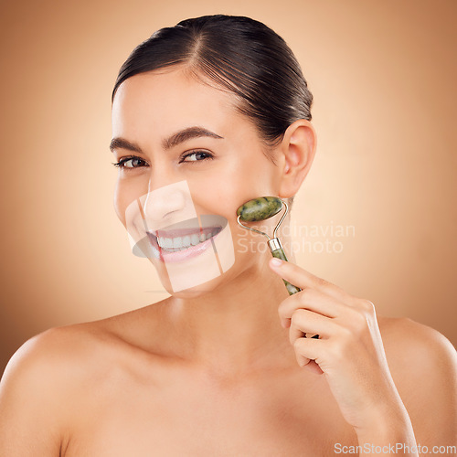 Image of Skincare, jade roller and portrait of woman in studio for beauty, wellness and anti aging against brown background. Facial, skin and girl relax with massaging tool, facelift and lymphatic drainage