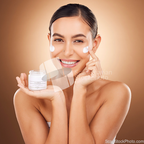 Image of Portrait, skincare and lotion with a model woman in studio on a brown background for beauty or hydration. Face, skin and cream with a happy young female holding a container to apply moisturizer