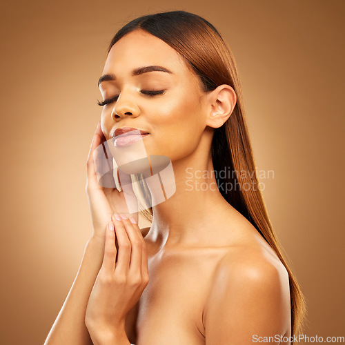 Image of Woman with hand on face, hair and skincare with bronze glow and luxury salon treatment on brown background. Beauty, makeup and skin care cosmetics, hispanic model with straight hairstyle in studio.