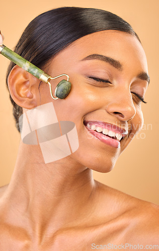 Image of Woman, face and beauty, roller and skincare, smile and facial massage on studio background. Jade quartz cosmetic tools, dermatology and skin glow, happy Indian female and self care with cosmetics