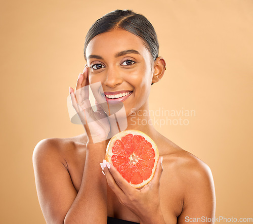 Image of Skincare, portrait and a woman with a grapefruit for a glow isolated on a studio background. Food, smile and an Indian model with a fruit for healthy skin, complexion and vitamin c treatment