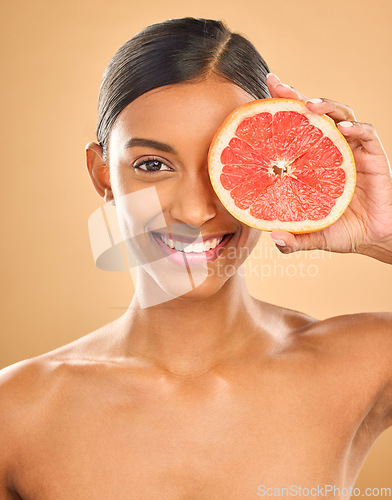 Image of Face smile, skincare and woman with grapefruit in studio isolated on a brown background. Portrait, natural cosmetics and happy Indian female model with citrus fruit for vitamin c, nutrition or beauty